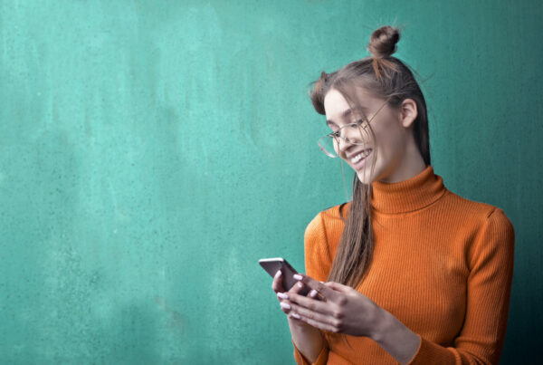 vrouw houdt lachend haar telefoon vast op een groene achtergrond