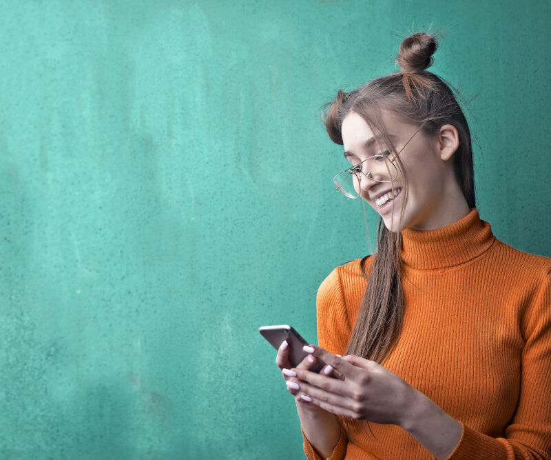vrouw houdt lachend haar telefoon vast op een groene achtergrond