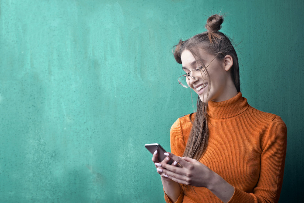 vrouw houdt lachend haar telefoon vast op een groene achtergrond
